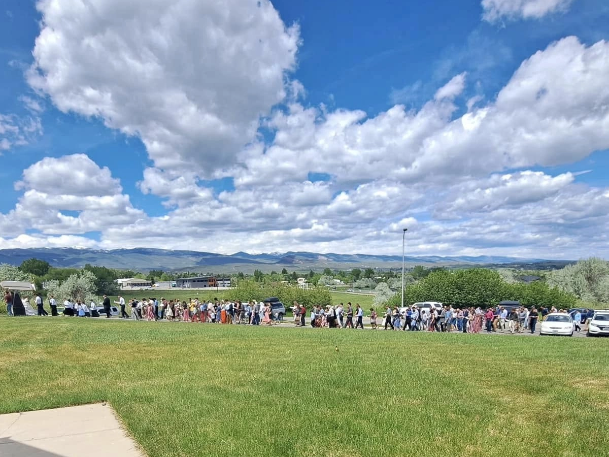 A long line of people participating in an outdoor procession across a grassy field.