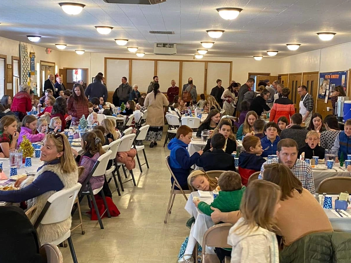 A crowded church fellowship hall with people dining at long tables.